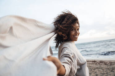 Happy woman holding scarf at beach - JOSEF17298