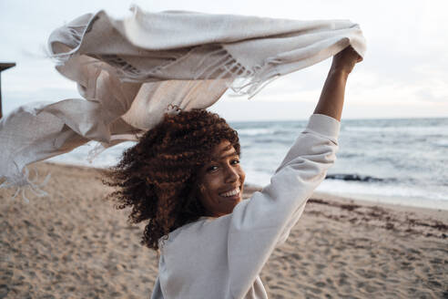 Cheerful woman holding scarf at beach - JOSEF17299