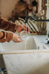 Hände eines Mannes beim Reinigen eines Plastikbehälters im Spülbecken einer Küche - VSNF00552