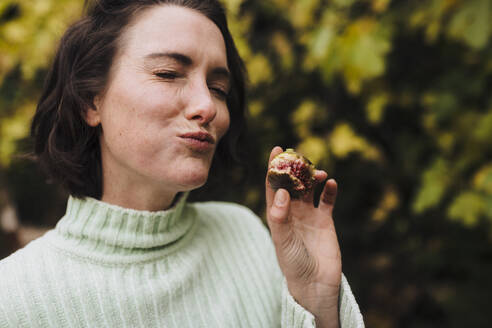 Woman with eyes closed eating fig in back yard - JOSEF17338