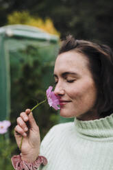 Lächelnde Frau riecht an einer Blume im Hinterhof - JOSEF17341