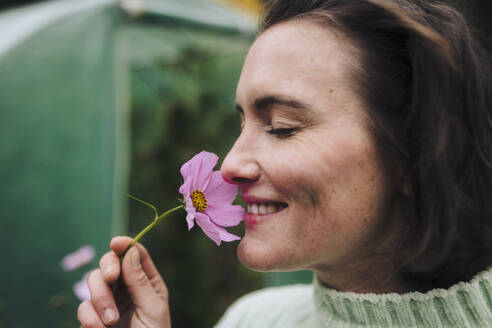 Happy woman smelling pink flower - JOSEF17343