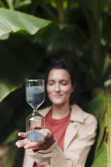 Frau mit Sanduhr vor einem Bananenbaum stehend - JOSEF17401