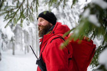 Sanitäter des Bergrettungsdienstes, der im Winter im Wald spazieren geht und spricht. - HPIF06076