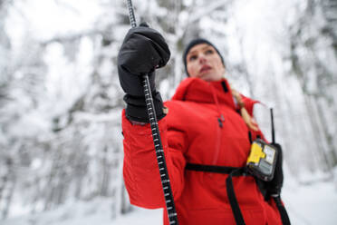 Tiefblick auf eine Bergwachtfrau bei einem Einsatz im Winter im Wald, um eine Person nach einem Lawinenabgang zu finden. - HPIF06097