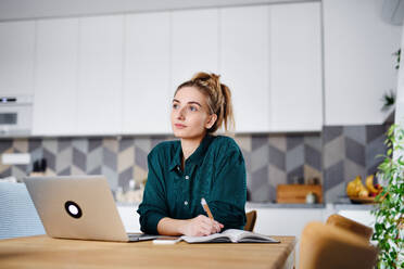 Eine junge Studentin mit Laptop, die zu Hause Notizen schreibt, Home Office und Lernen. - HPIF06137