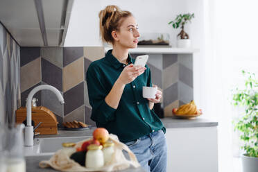 Ein Porträt einer jungen Studentin, die zu Hause einen Kaffee trinkt und ein Smartphone benutzt. - HPIF06147