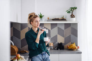 Ein Porträt einer jungen Studentin, die zu Hause einen Kaffee trinkt und ein Smartphone benutzt. - HPIF06148