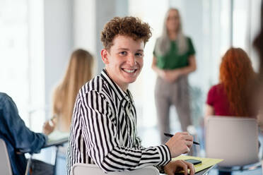 Ein Porträt einer jungen Studentin, die in einem Klassenzimmer sitzt und in die Kamera schaut. - HPIF06167