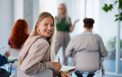 A portrait of young university student sitting in classroom indoors, looking at camera. - HPIF06170