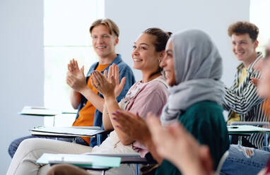 Ein Porträt einer fröhlichen Studentin, die in einem Klassenzimmer sitzt und lernt und klatscht. - HPIF06176