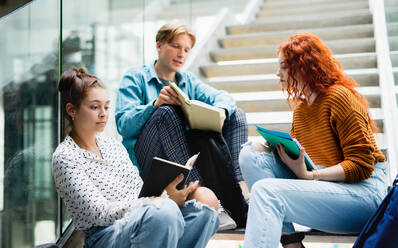 Fröhliche Universitätsstudenten, die auf einer Treppe sitzen und sich drinnen unterhalten, Konzept 