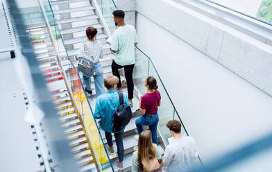 Eine Rückansicht von Universitätsstudenten, die die Treppe in einem Gebäude hinaufgehen, in die Kamera schauen und winken. - HPIF06191