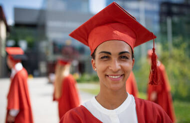 Ein Porträt eines fröhlichen Universitätsstudenten mit Kappe und Talar, der in die Kamera schaut, Abschlusskonzept. - HPIF06231