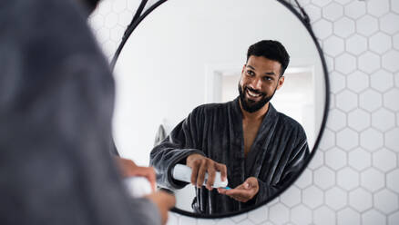 Portrait of young man using shaving gel indoors at home, morning or evening routine concept. - HPIF06249