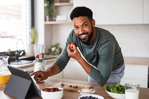 Portrait of young man with tablet preparing healthy breakfast indoors at home, home office concept. - HPIF06252