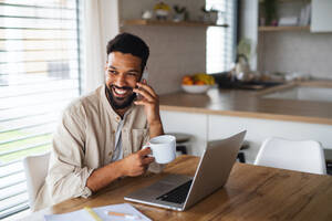 Glücklicher junger Mann Student mit Laptop und Smartphone arbeiten drinnen zu Hause, Home-Office-Konzept. - HPIF06254
