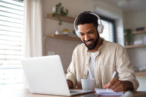 Porträt eines jungen Mannes mit Laptop und Kopfhörern zu Hause beim Lernen. - HPIF06255