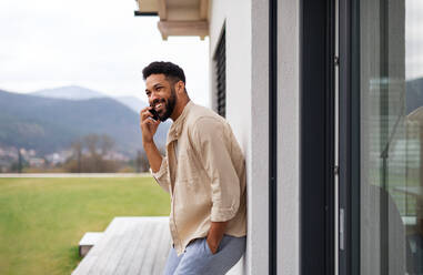 Portrait of young man student with smartphone outdoors on patio at home, making a phone call. - HPIF06257