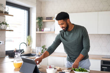 Porträt eines jungen Mannes mit Tablet, der zu Hause ein gesundes Frühstück zubereitet, Home-Office-Konzept. - HPIF06276