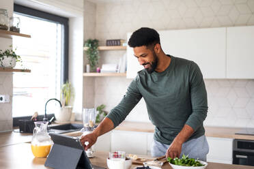 Portrait of young man with tablet preparing healthy breakfast indoors at home, home office concept. - HPIF06276