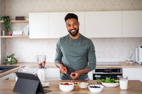 Porträt eines jungen Mannes mit Tablet, der zu Hause ein gesundes Frühstück zubereitet, Home-Office-Konzept. - HPIF06277
