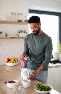 Portrait of young man with tablet preparing healthy breakfast indoors at home, making milk shake. - HPIF06278