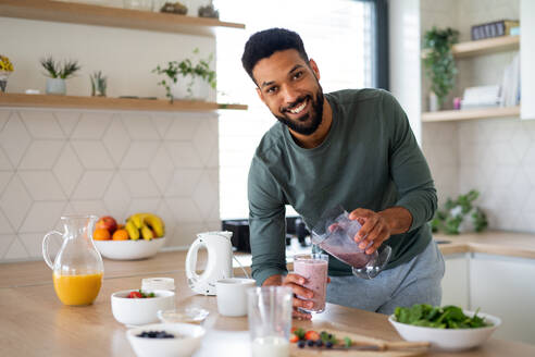 Portrait of young man preparing healthy breakfast indoors at home, looking at camera. - HPIF06280