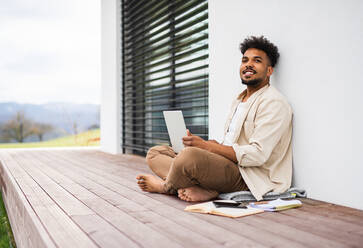 Ein junger Mann Student mit Laptop sitzen auf der Terrasse im Freien zu Hause, Studium. - HPIF06301