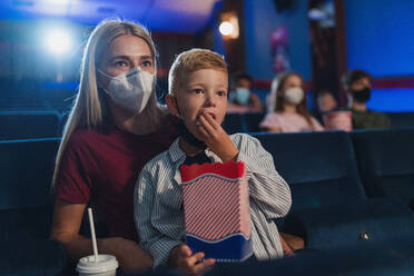 Ein kleiner Junge mit seiner Mutter isst Popcorn im Kino und sieht sich Filme und das Coronavirus-Konzept an. - HPIF06302