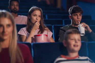 Frontansicht eines fröhlichen jungen Paares mit Getränk und Popcorn im Kino, das sich einen Film ansieht. - HPIF06303