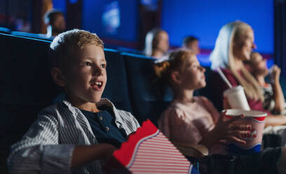 Ein kleiner Junge mit seiner Familie sitzt im Kino und sieht sich einen Film an, isst Popcorn - HPIF06308