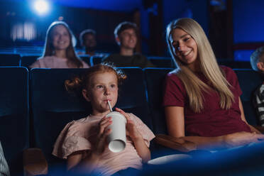 Eine Mutter mit glücklichen kleinen Kindern im Kino, die einen Film ansehen und mit einem Strohhalm trinken. - HPIF06313