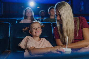 Ein glückliches kleines Mädchen mit seiner Mutter im Kino, das sich einen Film ansieht. - HPIF06314