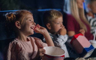 Ein kleines Mädchen mit Familie sitzt im Kino und sieht sich einen Film an, isst Popcorn - HPIF06322
