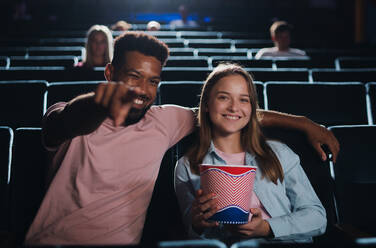Vorderansicht eines fröhlichen jungen Paares im Kino, das auf die Kamera zeigt. - HPIF06325