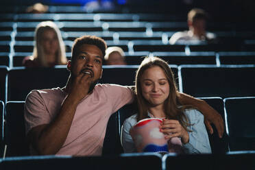 Frontansicht eines fröhlichen jungen Paares mit Popcorn im Kino, das sich einen Film ansieht. - HPIF06326
