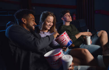Ein fröhliches junges Paar, das sich mit Popcorn im Kino unterhält. - HPIF06338