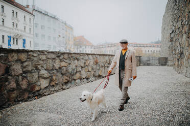 Ein glücklicher, eleganter älterer Mann geht mit seinem Hund in der Stadt spazieren. - HPIF06368