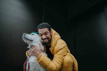 Ein glücklicher junger Mann umarmt seinen Hund im Freien im Winter vor dunklem Hintergrund. - HPIF06384