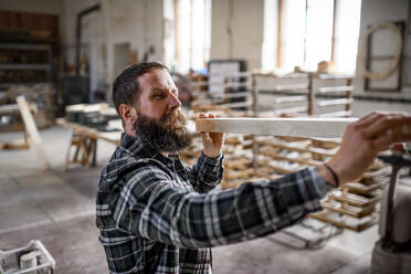 Ein reifer männlicher Schreiner trägt ein Holzbrett in einer Schreinerwerkstatt, ein kleines Geschäftskonzept. - HPIF06406