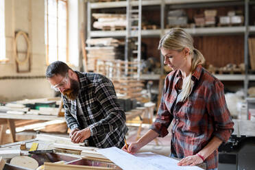 Two carpenters man and woman looking at blueprints indoors in a carpentery workshop. - HPIF06427