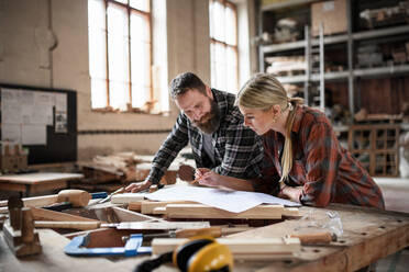 Zwei Tischler, ein Mann und eine Frau, sehen sich in einer Tischlerwerkstatt Baupläne an. - HPIF06435