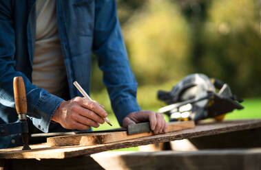 Nahaufnahme eines Handwerkers, der ein Brett misst, draußen im Garten. - HPIF06471