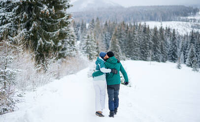 Rückansicht eines reifen Paares, das Arm in Arm im Freien in der winterlichen Natur des Tatra-Gebirges in der Slowakei spazieren geht. - HPIF06573