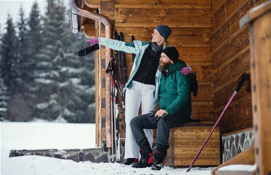 Glückliches reifes Paar, das sich bei einer Holzhütte in der winterlichen Natur ausruht, Skilanglauf. - HPIF06586