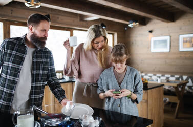 Glückliche Familie mit kleiner Tochter, die im Haus kocht, Winterurlaub in einer Privatwohnung. - HPIF06601