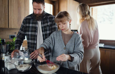 Glückliche Familie mit kleiner Tochter, die im Haus kocht, Winterurlaub in einer Privatwohnung. - HPIF06605