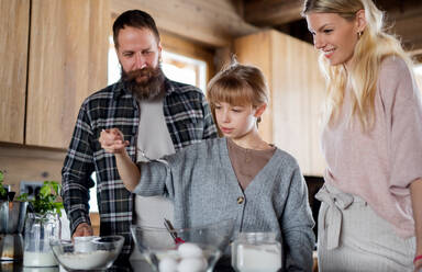 Glückliche Familie mit kleiner Tochter, die im Haus kocht, Winterurlaub in einer Privatwohnung. - HPIF06606