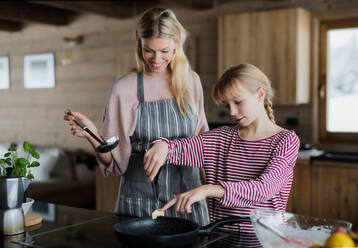 Glückliche Mutter mit kleiner Tochter beim Kochen im Haus, Winterurlaub in einer Privatwohnung. - HPIF06608